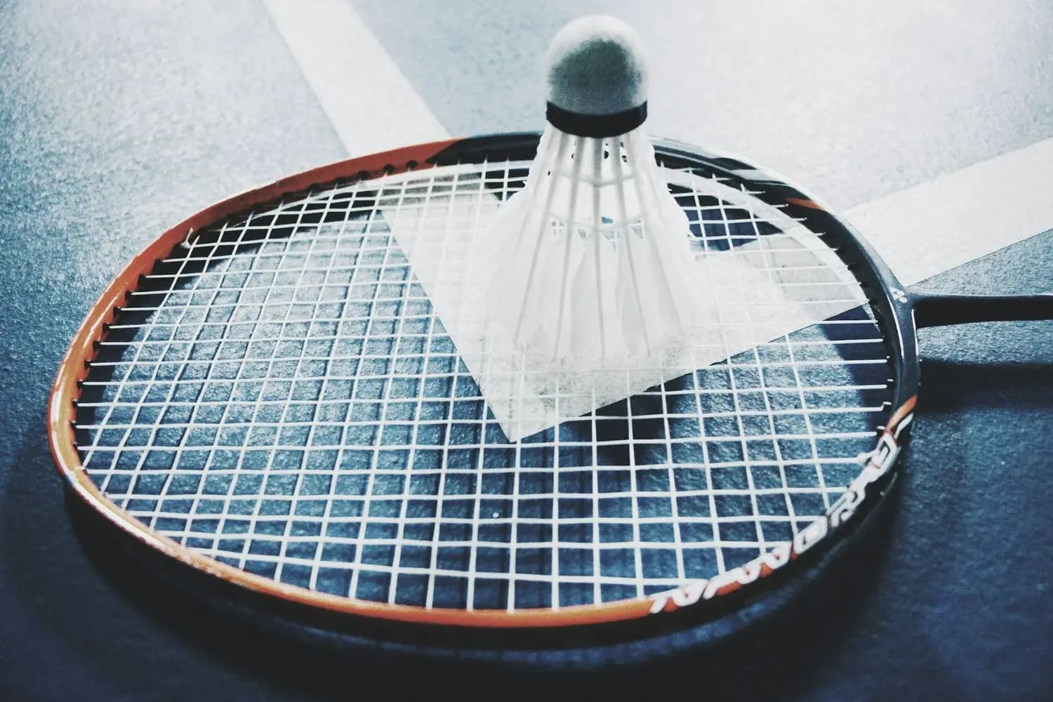 A badminton racket with a shuttlecock lying on a court