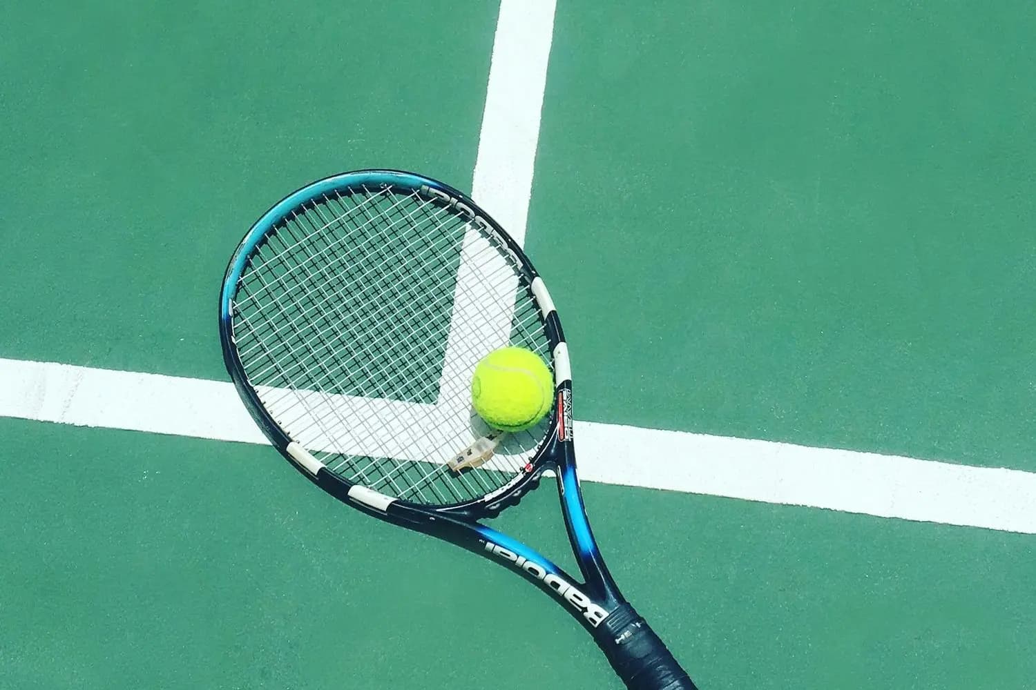 A tennis racket and ball by the line of a green court